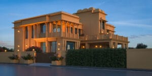 A side perspective of a regal villa designed by ARTILETT, featuring layered terraces, large glass windows, and lush landscaping, with warm lighting highlighting the intricate details of the traditional Indian-inspired architecture during twilight.