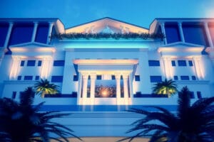 Luxury hotel exterior featuring white classical architecture with illuminated columns and palm trees at twilight