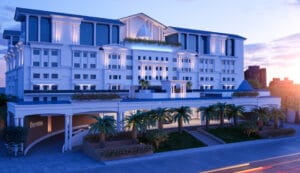 Luxury hotel exterior featuring white classical architecture with illuminated columns and palm trees at twilight